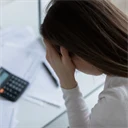 En kvinna håller sig för huvudet. Framför henne ligger räkningar och miniräknare.