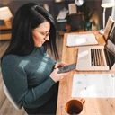 Kvinna sitter vid skrivbord med dator och mobiltelefon.