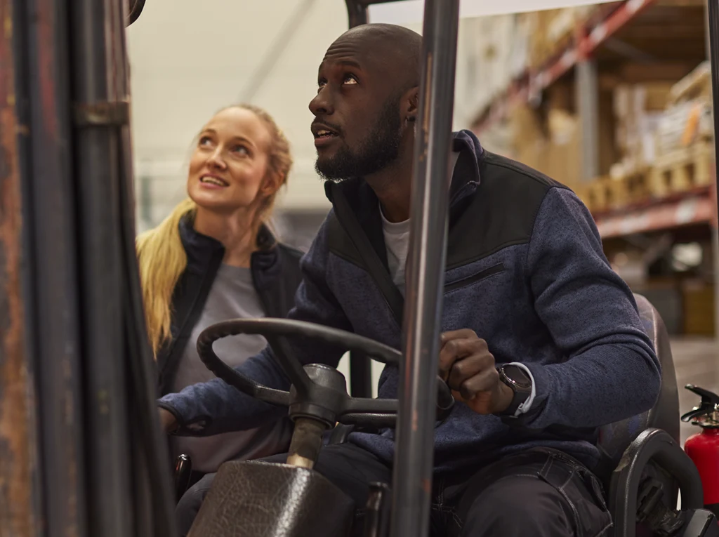 Manlig lagerarbetare som sitter i en truck samtalar med kvinnlig kollega.