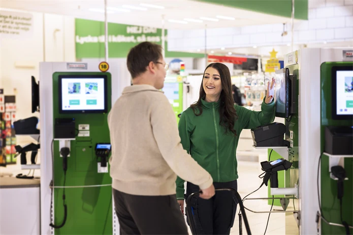 Ung kvinna hjälper en kund i självskanningen ien  butik